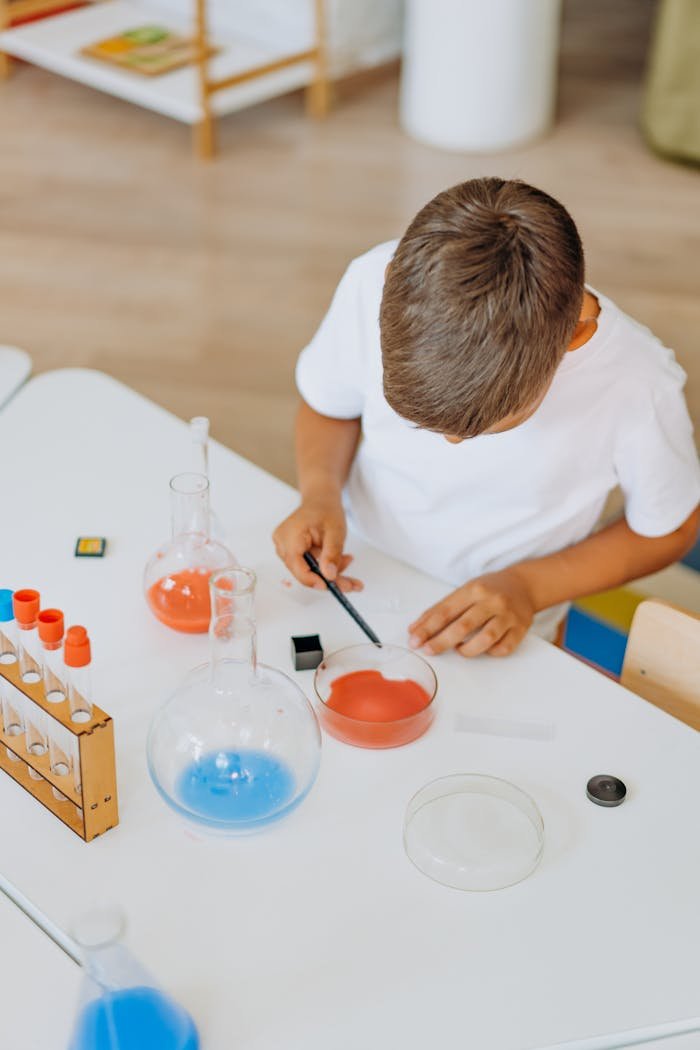 Child performing hands-on science experiment with colorful liquids in classroom setting.